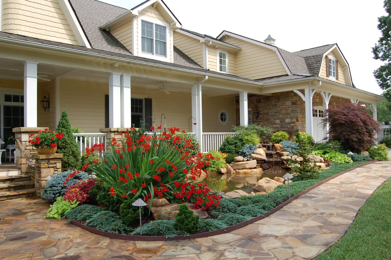 Covered porch elevation at the Silver Ridge estate with flowering beds and a stone path
