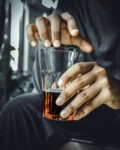 A vertical closeup of the man's hands holding a glass of beer.