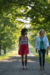 Two women walking down a path lined with trees.