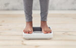 Closeup of young African American woman standing on scales indoors, checking her weight, cropped view of feet. Unrecognizable black lady on slimming diet. Healthcare concept