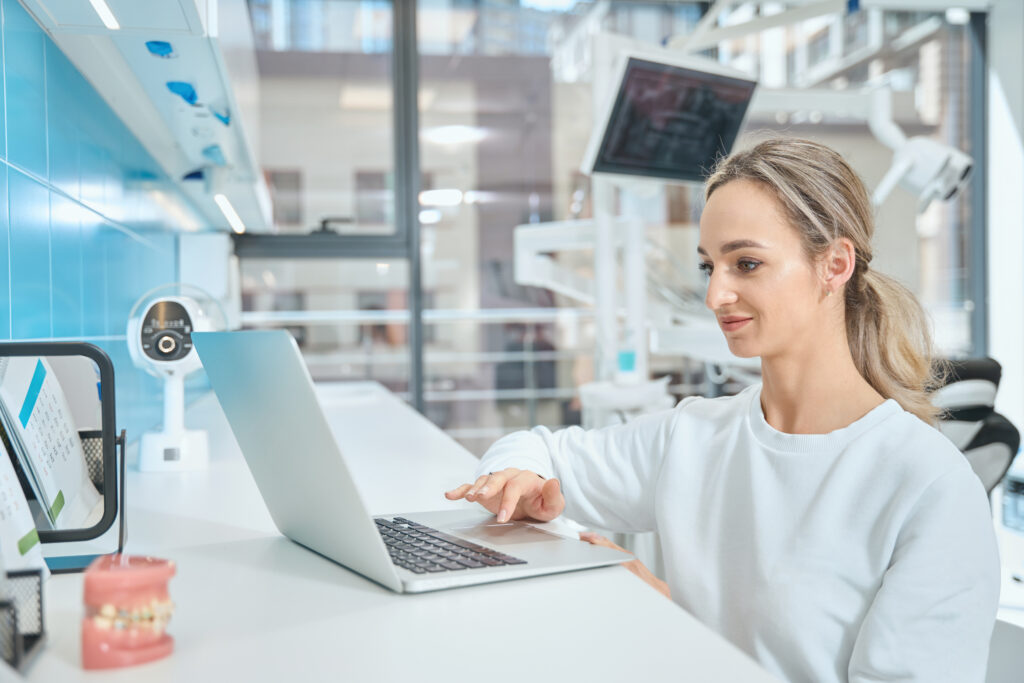 Smiling woman physician sitting on chair and using computer in the dentistry office