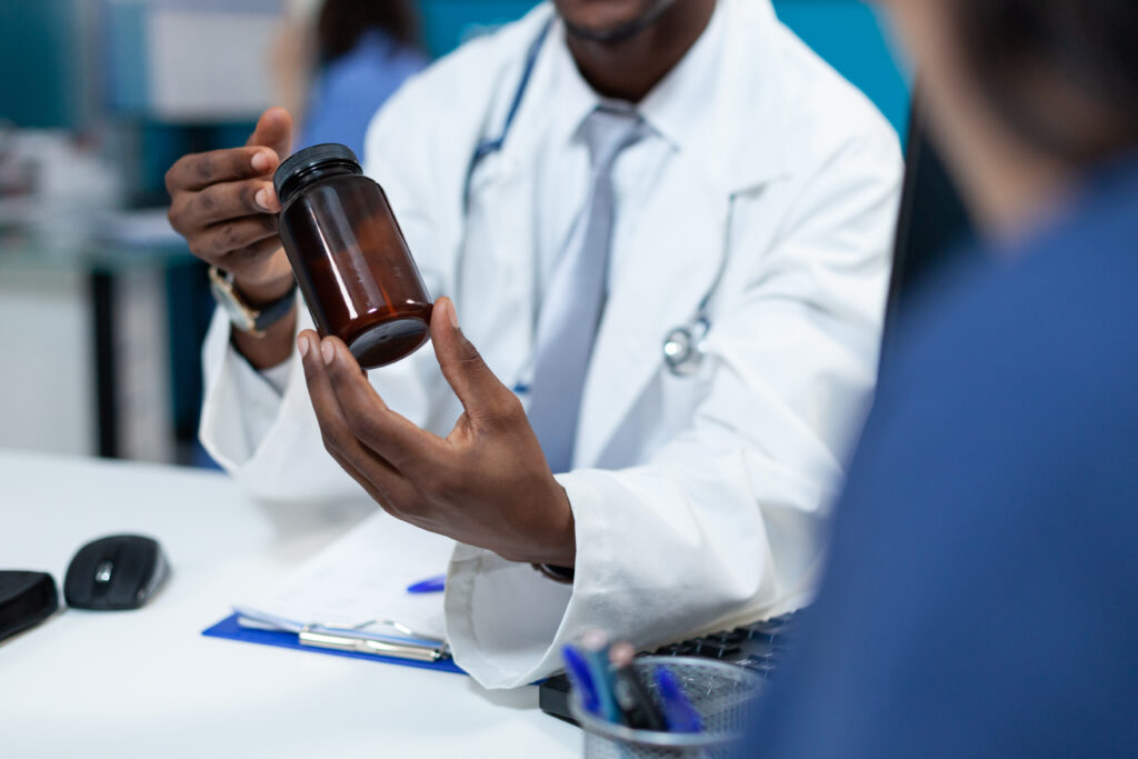 Closeup of african american pediatrician doctor holding pills bottle explaining medication treatment to patient mother during clinical appointment in hospital office. Medicine service