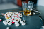 Junkie kit, narcotic concept, addiction problem. Pills are laid out on wooden table, alcohol and handcuff